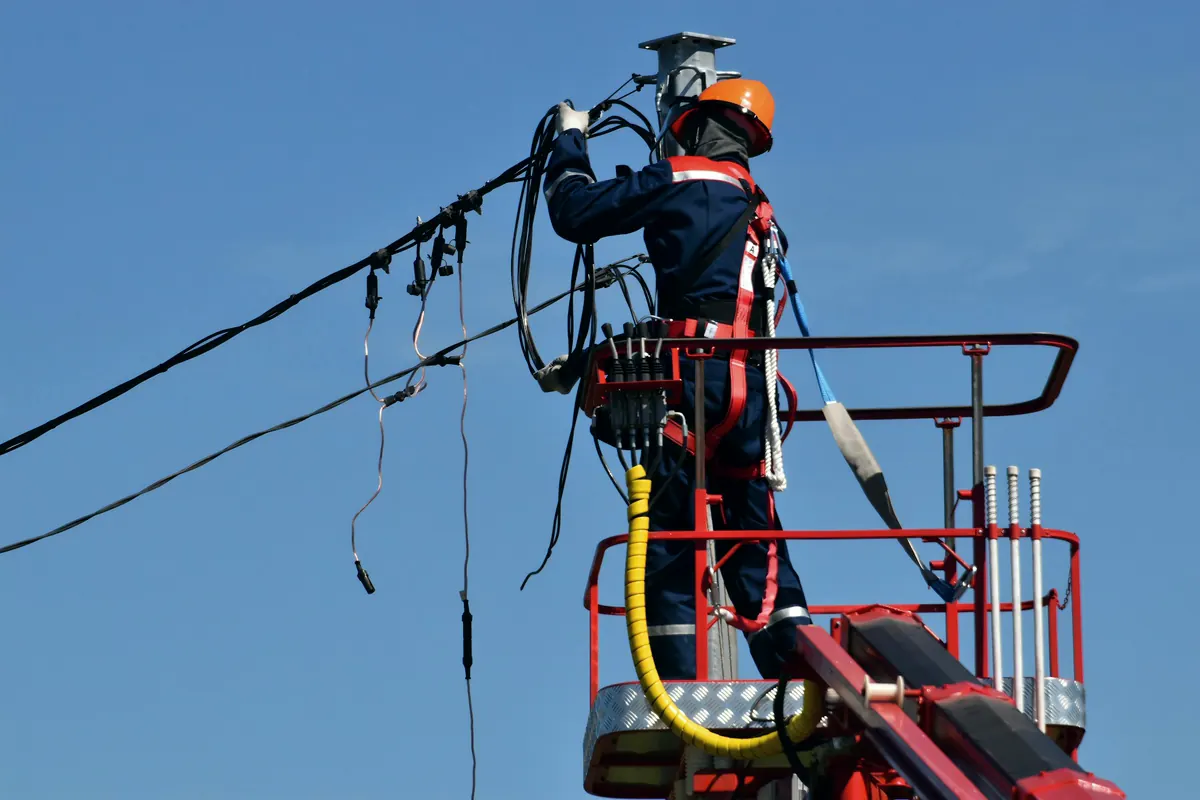 Técnico de la red eléctrica reparando cables en una grúa